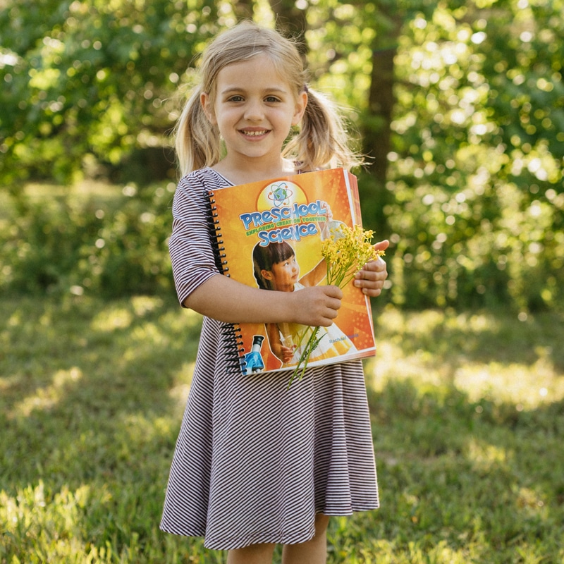 Apologia's Preschool Science Curriculum held by a young girl in the woods. 