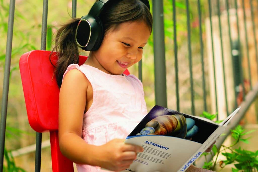 child listing to the audiobook of Exploring Creation with Astronomy 2nd edition while reading it